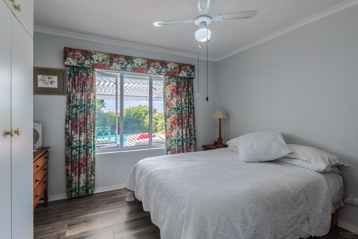 A bedroom featuring laminate flooring, a ceiling fan, and a built-in wardrobe, with a window view overlooking the outdoor pool area.