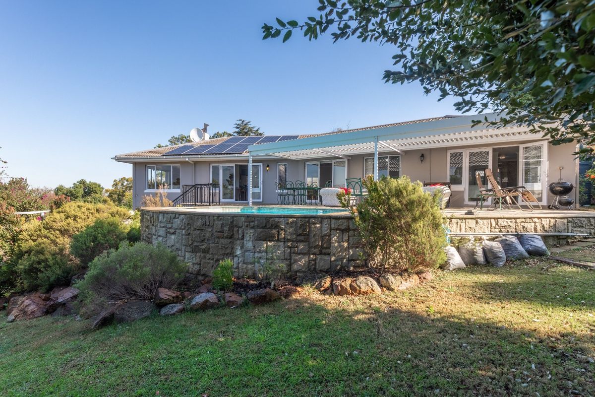 Rear view of the house featuring a swimming pool with a stone retaining wall, a covered patio area, and roof-mounted solar panels.