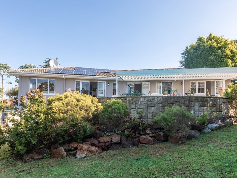 Rear view of the house featuring a stone retaining wall, a covered patio area, and roof-mounted solar panels set within a landscaped garden.