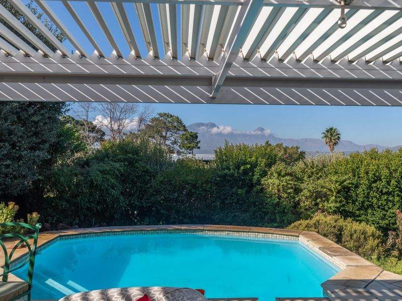 Outdoor pool area featuring a stone-edged swimming pool under a modern louvered pergola, offering scenic mountain views.