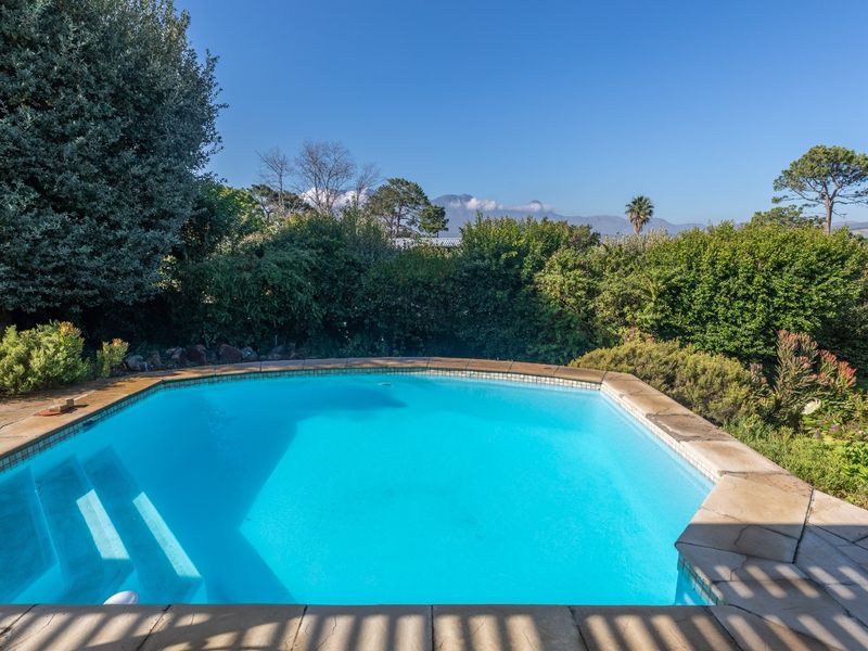 A well-maintained outdoor swimming pool featuring stone coping, set within a lush landscaped garden with scenic mountain views in the background.