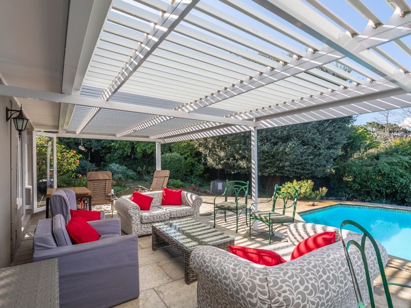 Covered outdoor patio featuring a modern louvred pergola, stone paving, and direct access to a private swimming pool and garden area.