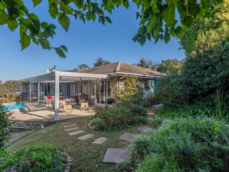 Rear view of the property featuring a landscaped garden, stone pathway, covered patio area, and a swimming pool.