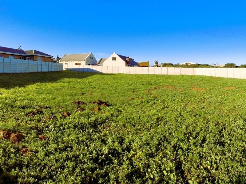 A vacant residential plot enclosed by precast concrete boundary walls, featuring a grassy surface ready for development.