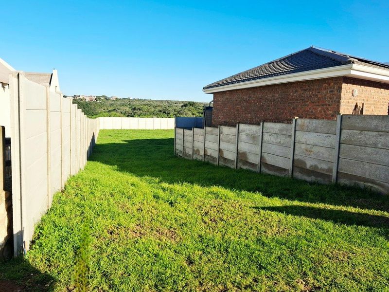 A view of the vacant residential land showing the grassed yard area enclosed by precast concrete boundary walls and adjacent brick dwelling.