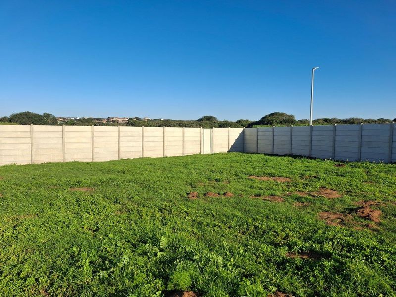 A vacant residential plot featuring a perimeter precast concrete wall and a street light pole, offering a clear space for future development.