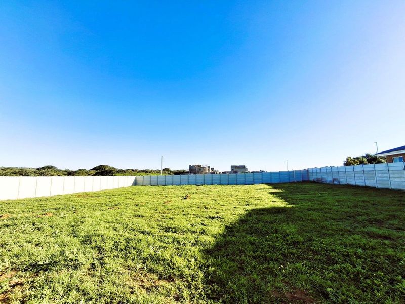 A vacant residential plot featuring level grass terrain and perimeter precast concrete walling, offering a clear space ready for development.