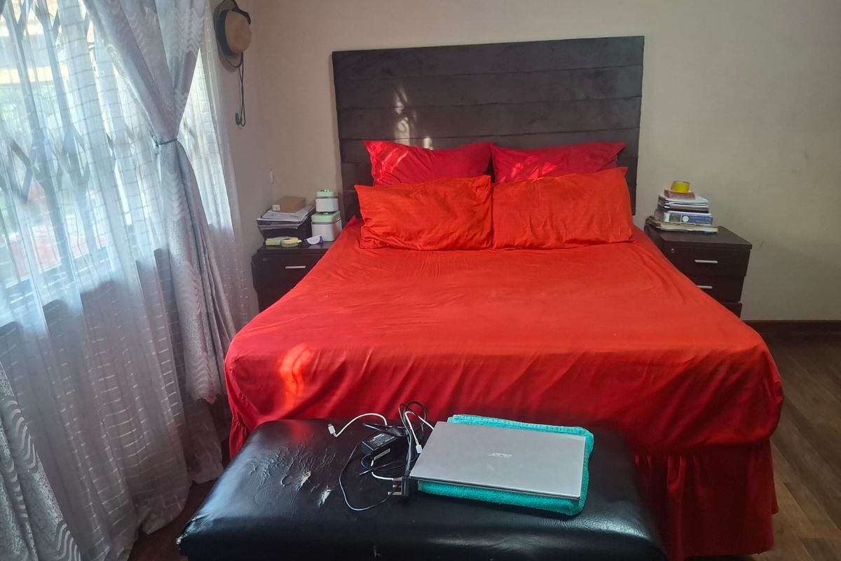 A bedroom featuring wooden flooring and a window with security bars.
