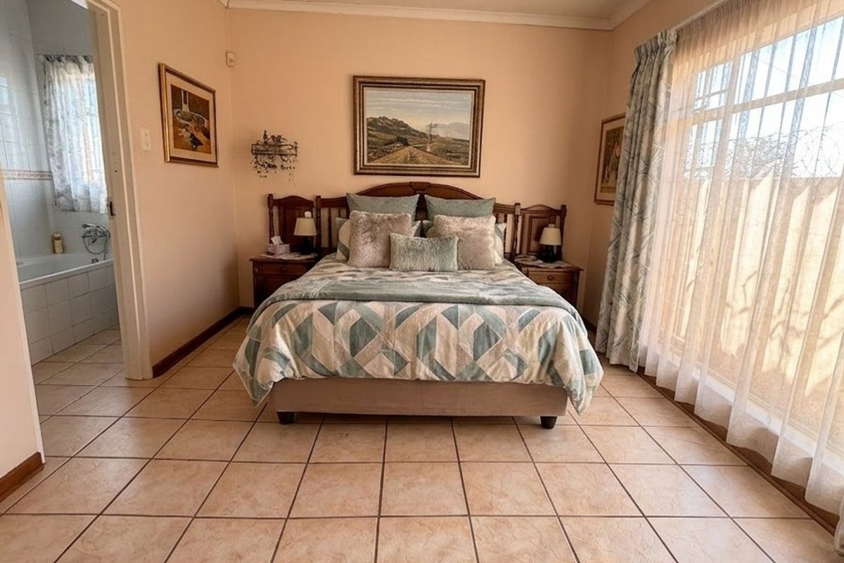 A spacious bedroom featuring ceramic floor tiles, recessed lighting, and direct access to an en-suite bathroom, with large windows providing natural light.
