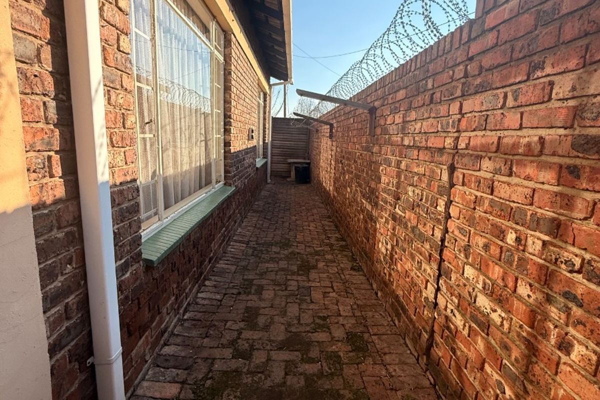 A narrow side passage featuring brick paving and a high brick boundary wall secured with razor wire.
