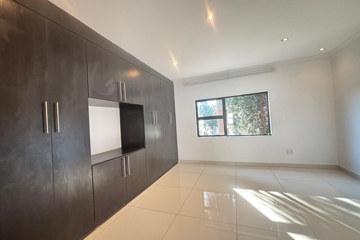 A bright, empty bedroom featuring large dark wood built-in cupboards, polished floor tiles, and recessed ceiling lighting.