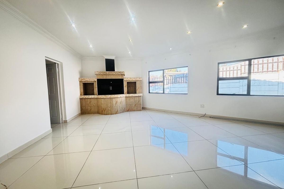 Spacious living area featuring large format floor tiles, recessed downlighting, and a built-in indoor braai fireplace with tiled surround.