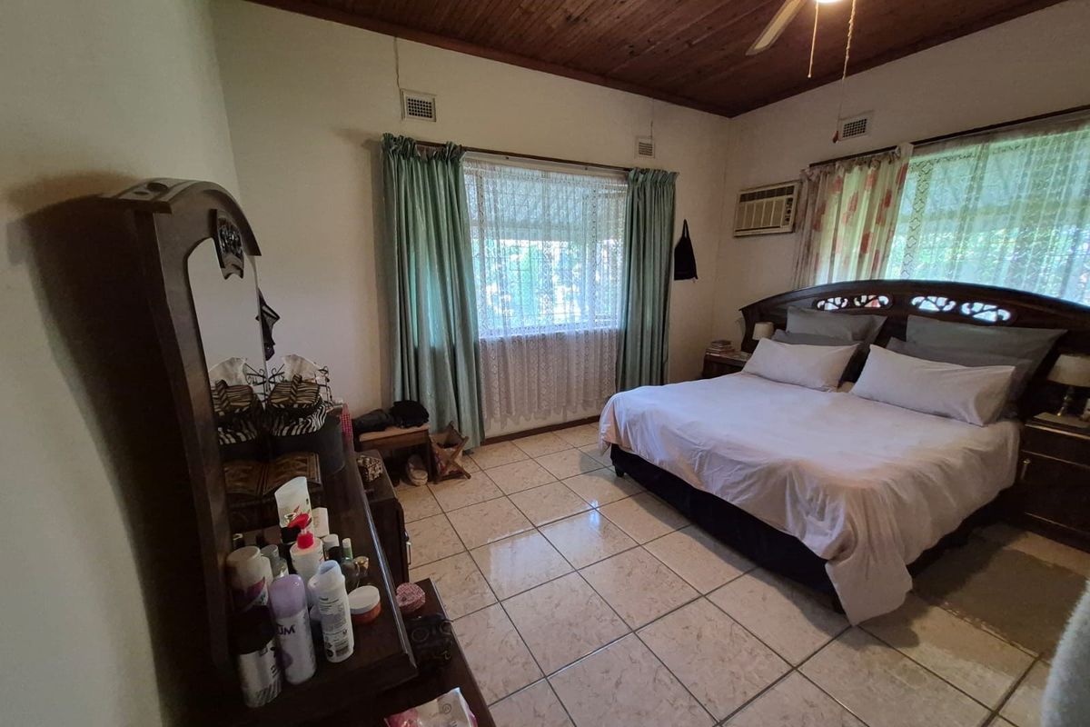 A spacious bedroom featuring tiled flooring, a timber-paneled ceiling, a ceiling fan, and a built-in window air conditioning unit.