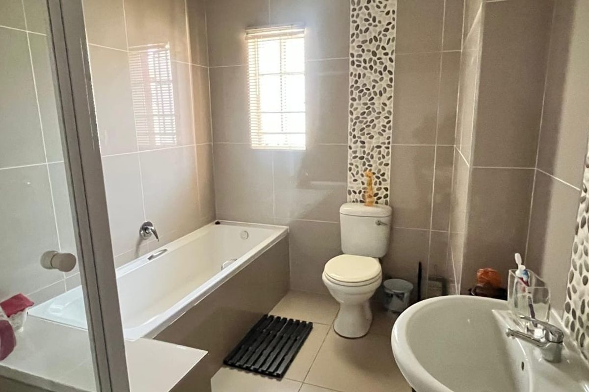 A functional bathroom featuring a built-in bathtub, a pedestal sink, and a toilet, accented with decorative pebble-style wall tiling.