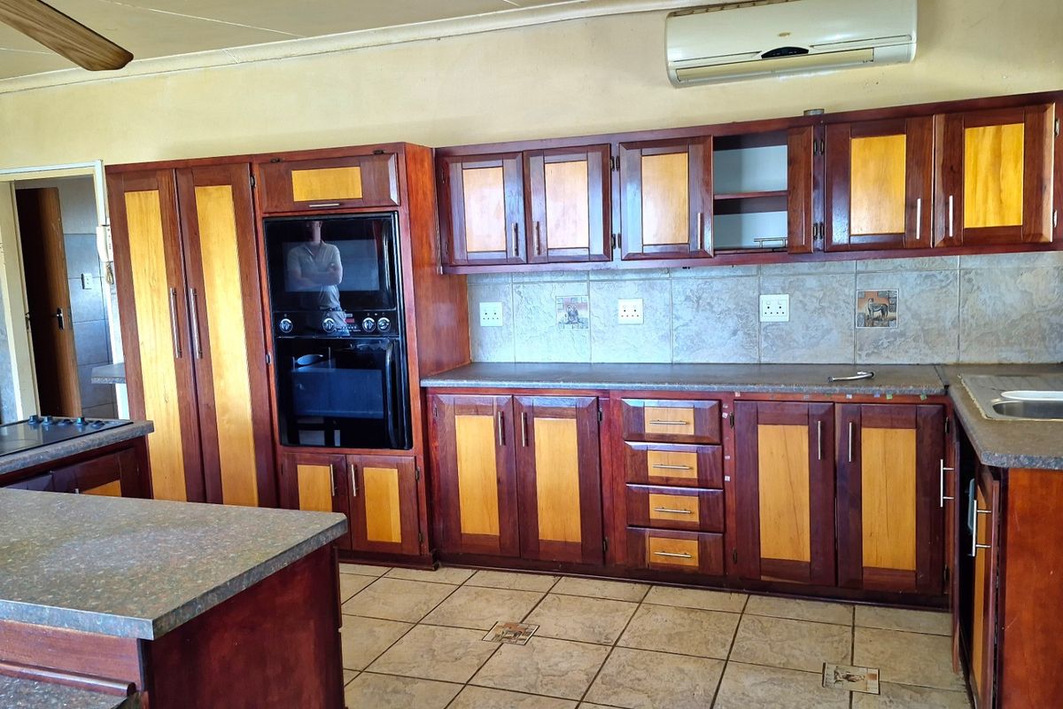 A spacious kitchen featuring two-tone wooden cabinetry, built-in oven and microwave, stone countertops, and tiled flooring, offering a functional layout with ample storage space.