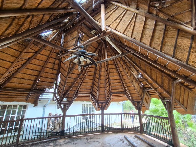 An outdoor thatched-roof patio area featuring exposed timber beams and metal railings, currently requiring significant maintenance and repair to the roof structure.