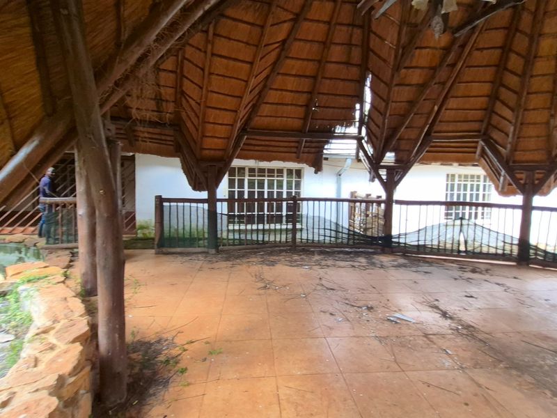 A large covered patio area featuring a traditional thatched roof, timber support beams, and tiled flooring, currently requiring maintenance and repair.