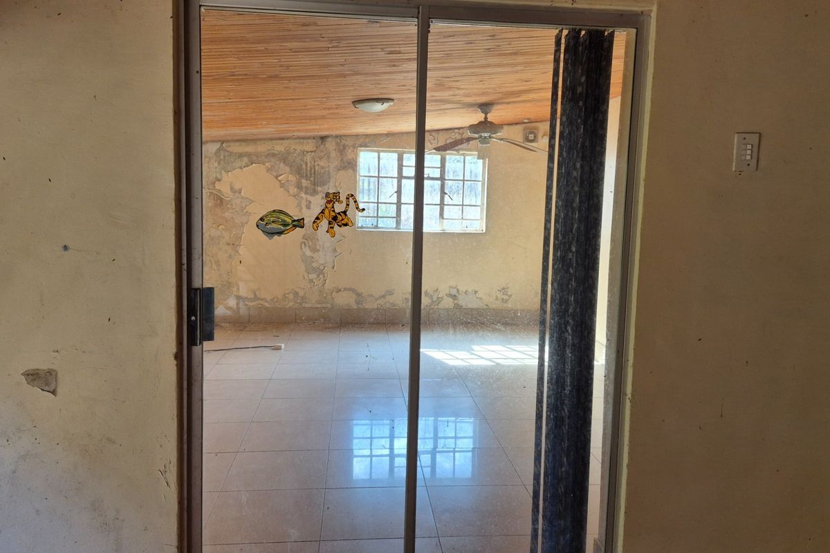 An empty living room featuring tiled floors, a timber ceiling, and a sliding glass door, currently requiring significant wall repairs and cosmetic updates.