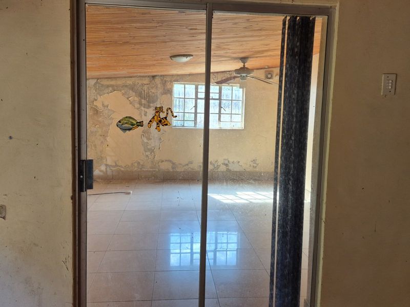 An empty living room featuring tiled floors, a timber ceiling, and a sliding glass door, currently requiring significant wall repairs and cosmetic updates.
