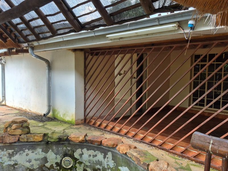 Outdoor pool area featuring a stone-clad pool edge, tiled patio, and a covered thatch structure with visible wear and maintenance requirements.