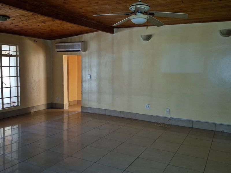 Spacious living area featuring a timber ceiling, tiled floors, ceiling fan, and wall-mounted air conditioning unit, offering a blank canvas for interior design.