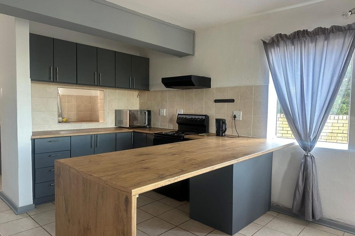 A functional kitchen featuring dark grey cabinetry, a wood-look breakfast bar, tiled backsplash, and a built-in extractor fan.
