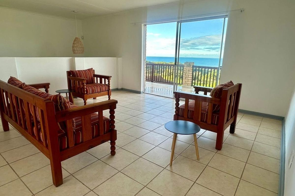 A bright living room featuring tiled flooring and large sliding glass doors that open onto a balcony with expansive ocean views.