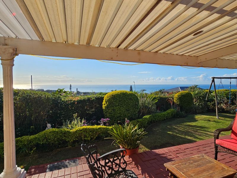 Covered patio area featuring brick paving and expansive ocean views overlooking a landscaped garden.