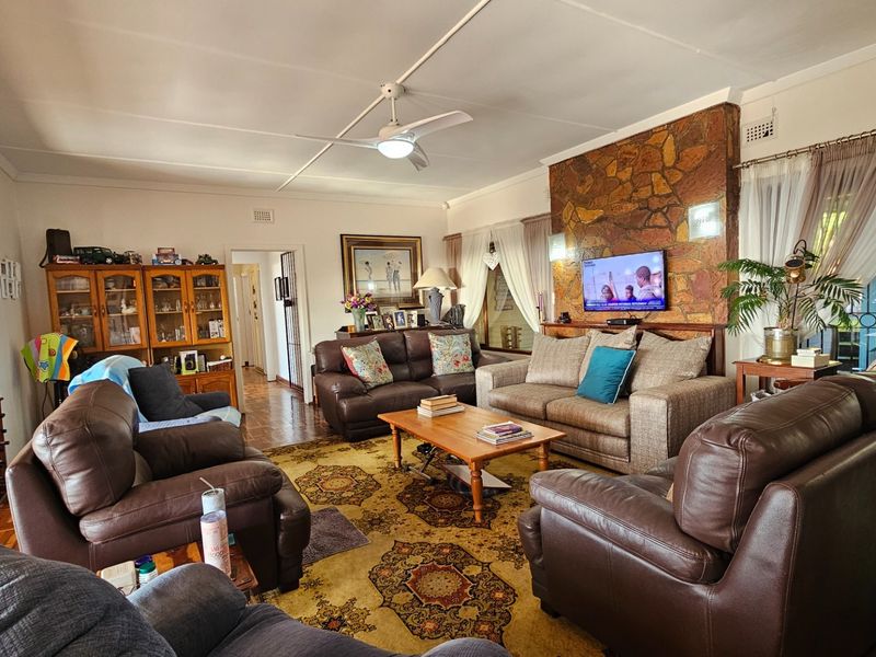 Spacious living room featuring a prominent stone-clad fireplace, ceiling fan, and large windows providing natural light and access to the outdoor area.