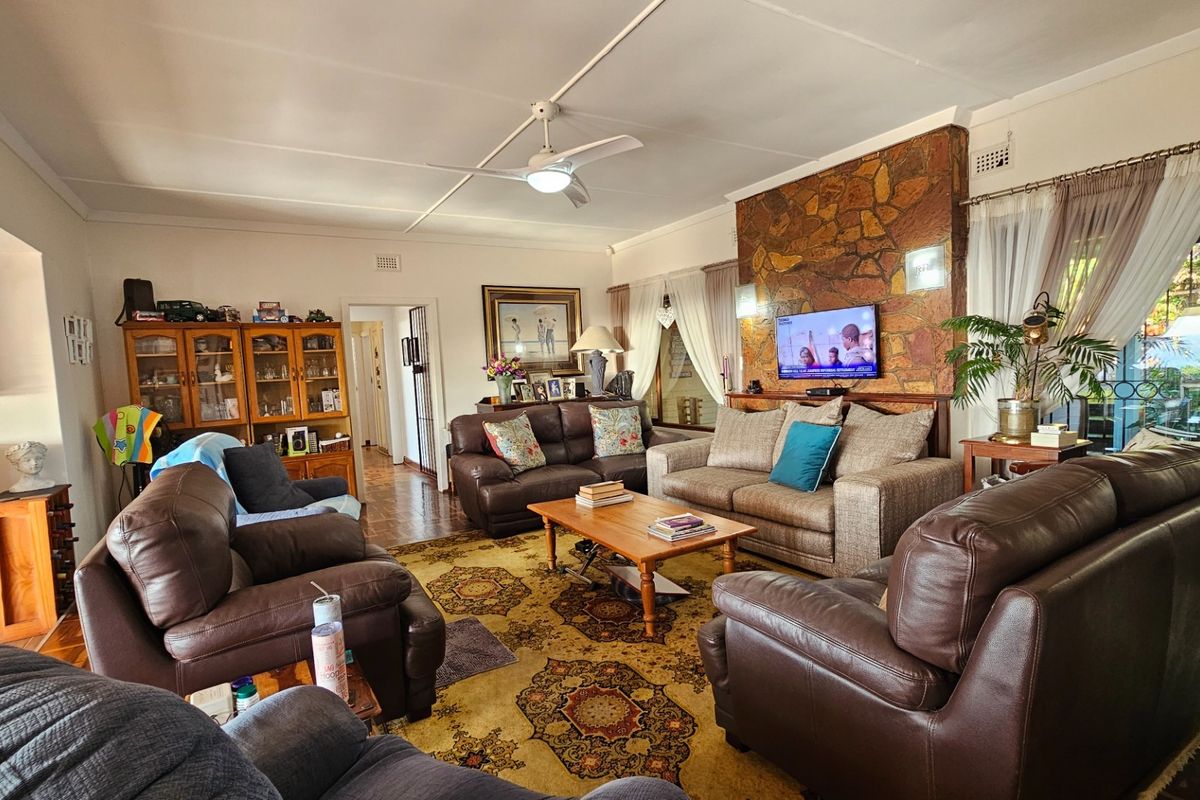 Spacious living room featuring a prominent stone-clad fireplace, ceiling fan, and large windows providing natural light and access to the outdoor area.