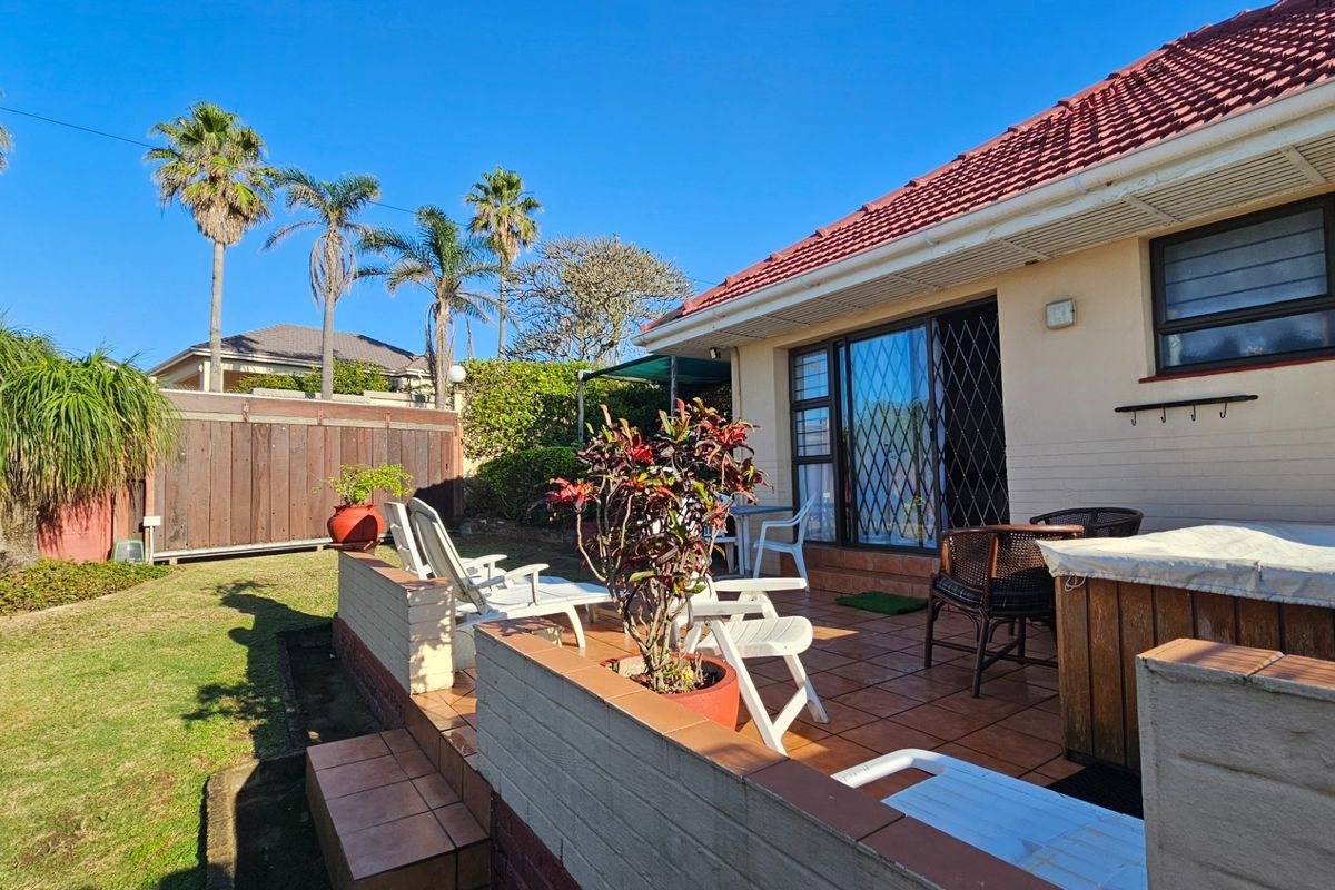 A rear patio area featuring tiled flooring, low brick retaining walls, and direct access to the garden through sliding glass doors.