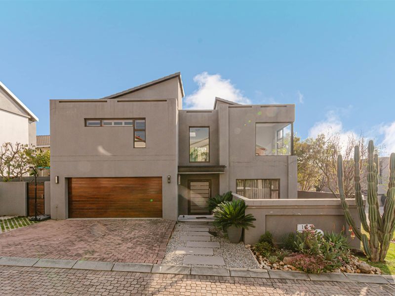 Modern double-story residential home featuring a contemporary grey facade, timber garage door, and a landscaped front garden with a paved driveway.