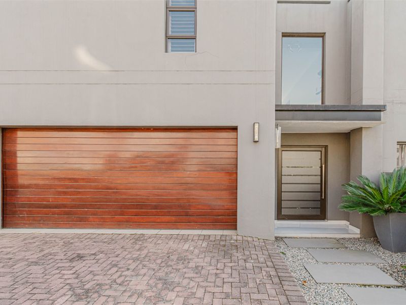 Modern front facade featuring a wooden garage door, paved driveway, and a contemporary entrance with stone pathway.