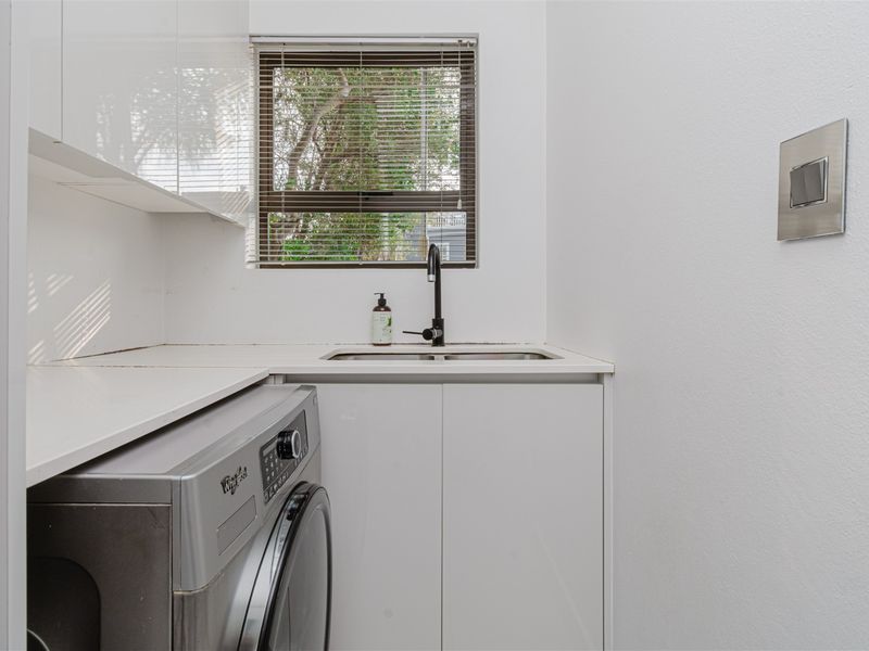 A functional laundry area featuring white built-in cabinetry, a stainless steel sink with a modern black tap, and space for a washing machine.