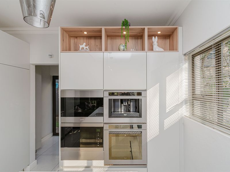Modern kitchen wall featuring high-gloss cabinetry, integrated appliances including an oven, microwave, and coffee machine, with stylish open shelving above.