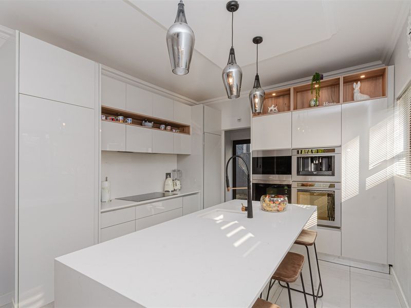 Modern kitchen featuring high-gloss white cabinetry, a central island with stone countertop, integrated appliances, and stylish pendant lighting.