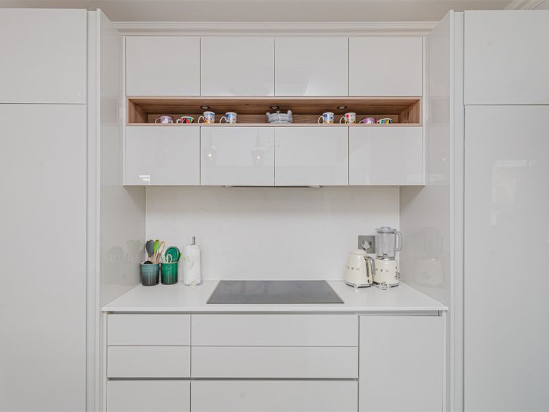 Modern kitchen featuring sleek white cabinetry, a stone countertop, and a built-in induction cooktop with integrated extractor fan.