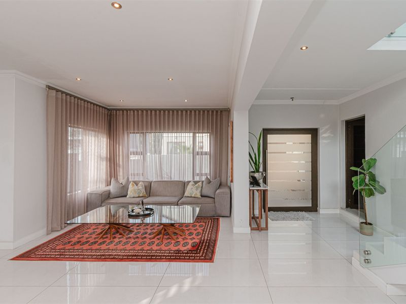 A bright and modern living area featuring polished tiled floors, recessed lighting, and a contemporary glass balustrade leading to an upper level.
