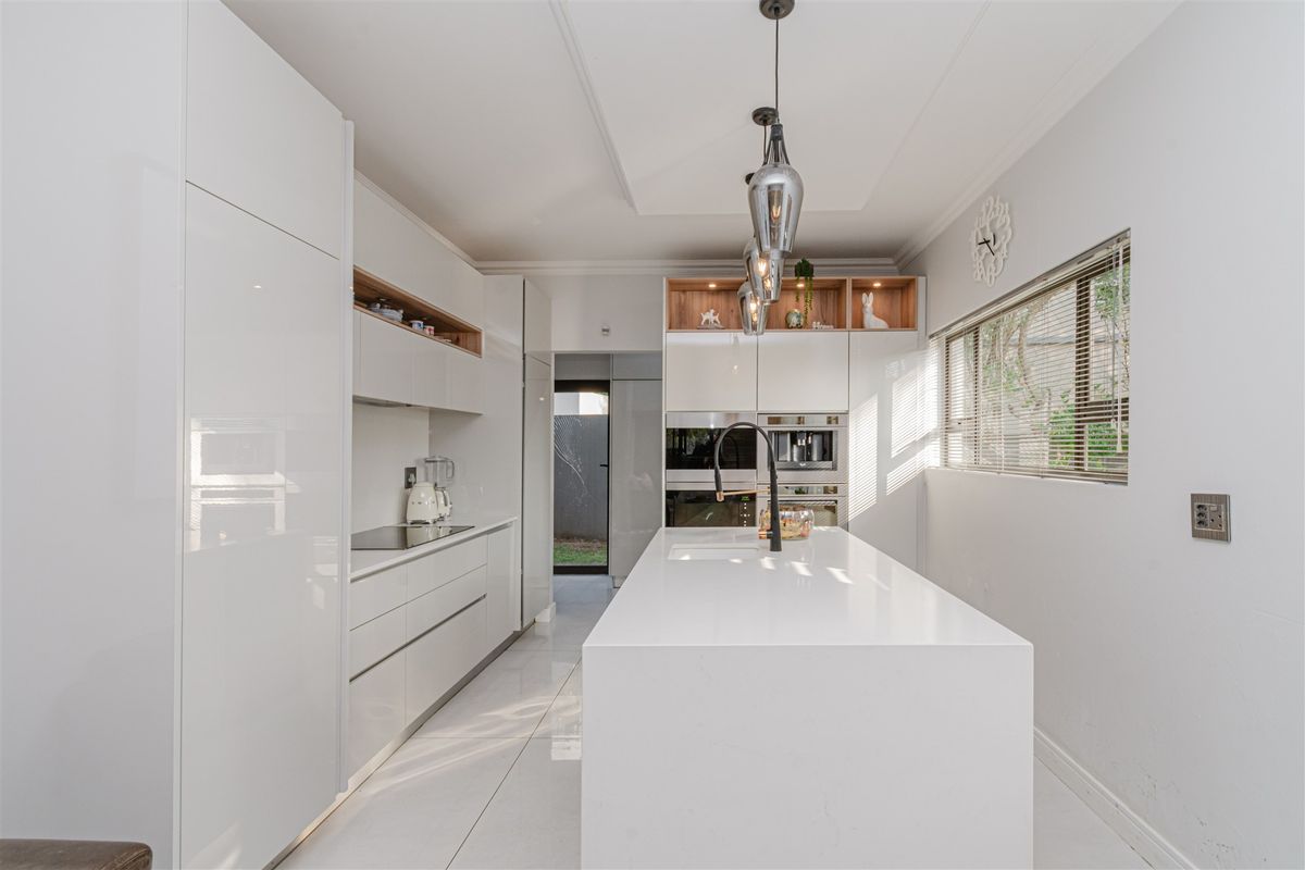 Modern, high-end kitchen featuring a large central island with quartz countertops, integrated appliances, sleek white cabinetry, and contemporary pendant lighting.