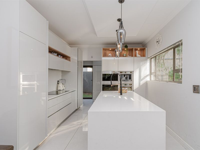 Modern, high-end kitchen featuring a large central island with quartz countertops, integrated appliances, sleek white cabinetry, and contemporary pendant lighting.
