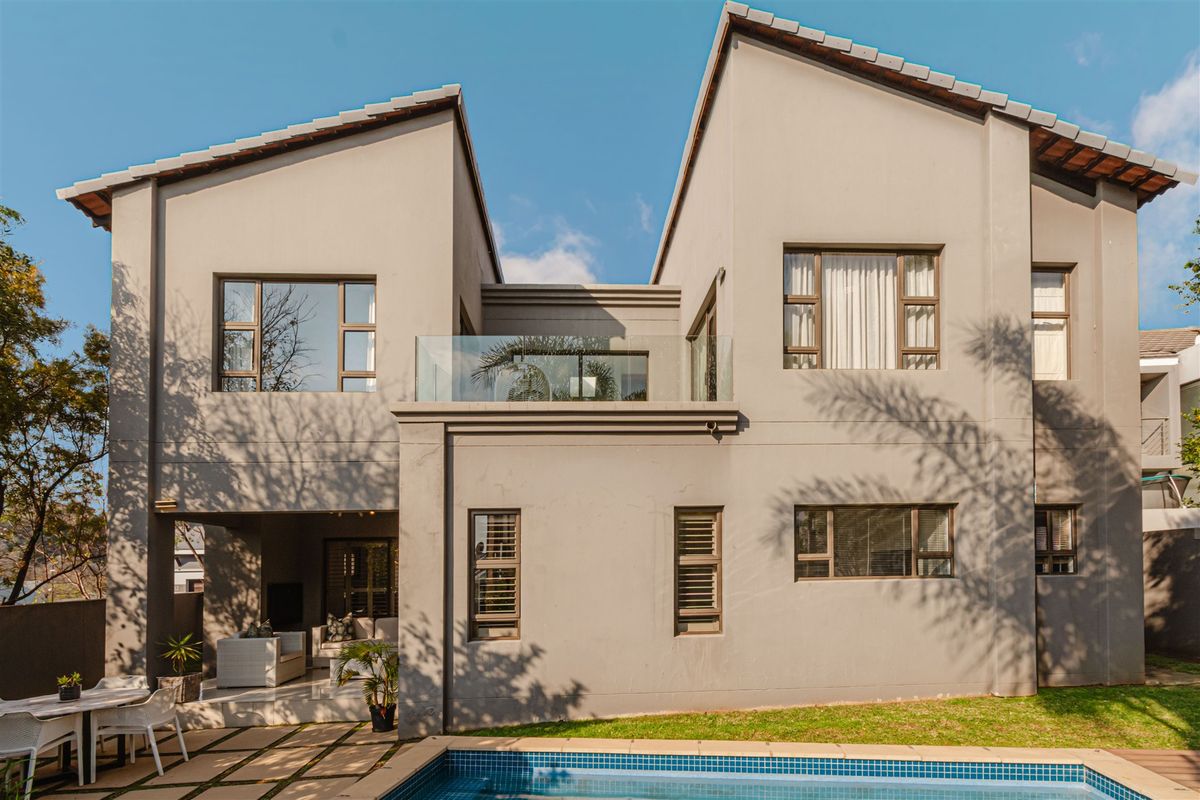 Rear view of a modern double-storey house featuring a swimming pool, covered patio area, and an upper-level balcony with glass balustrades.