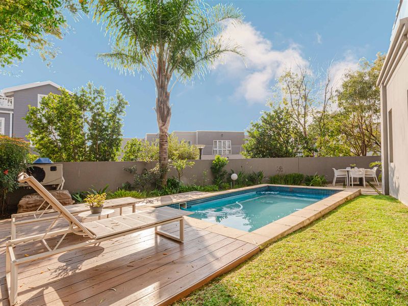 A well-maintained outdoor pool area featuring a swimming pool, timber decking, and a landscaped garden with a boundary wall.