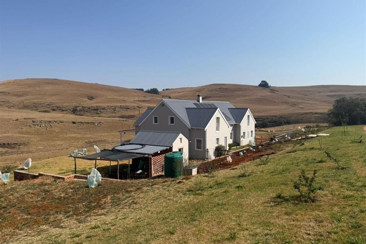 An elevated view of a rural residential property featuring a multi-gabled house with a metal roof, solar panels, and an attached outdoor patio area.