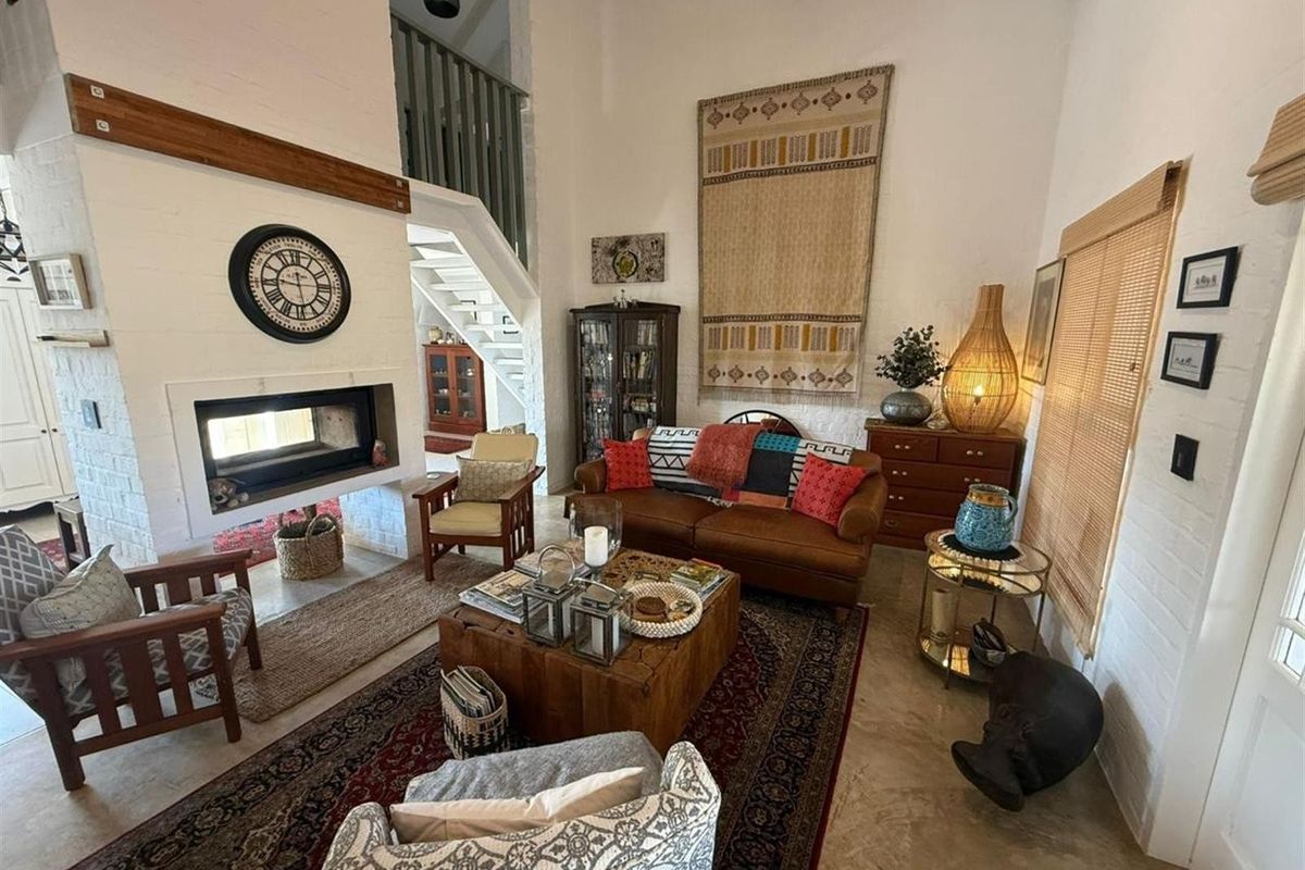 Spacious living room featuring a double-volume ceiling, a prominent built-in fireplace with a brick surround, and a staircase leading to an upper level.