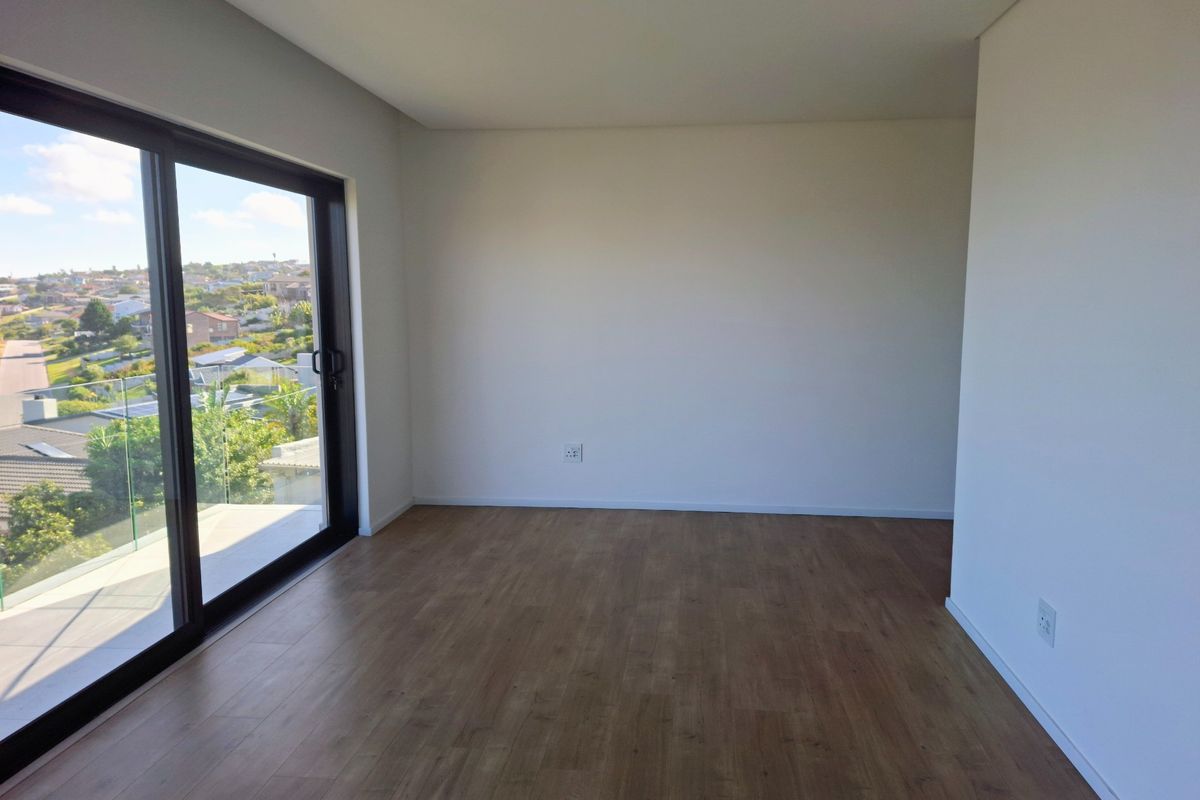 A bright, empty bedroom featuring modern laminate flooring, recessed lighting, and a large sliding glass door opening to a balcony with scenic views.
