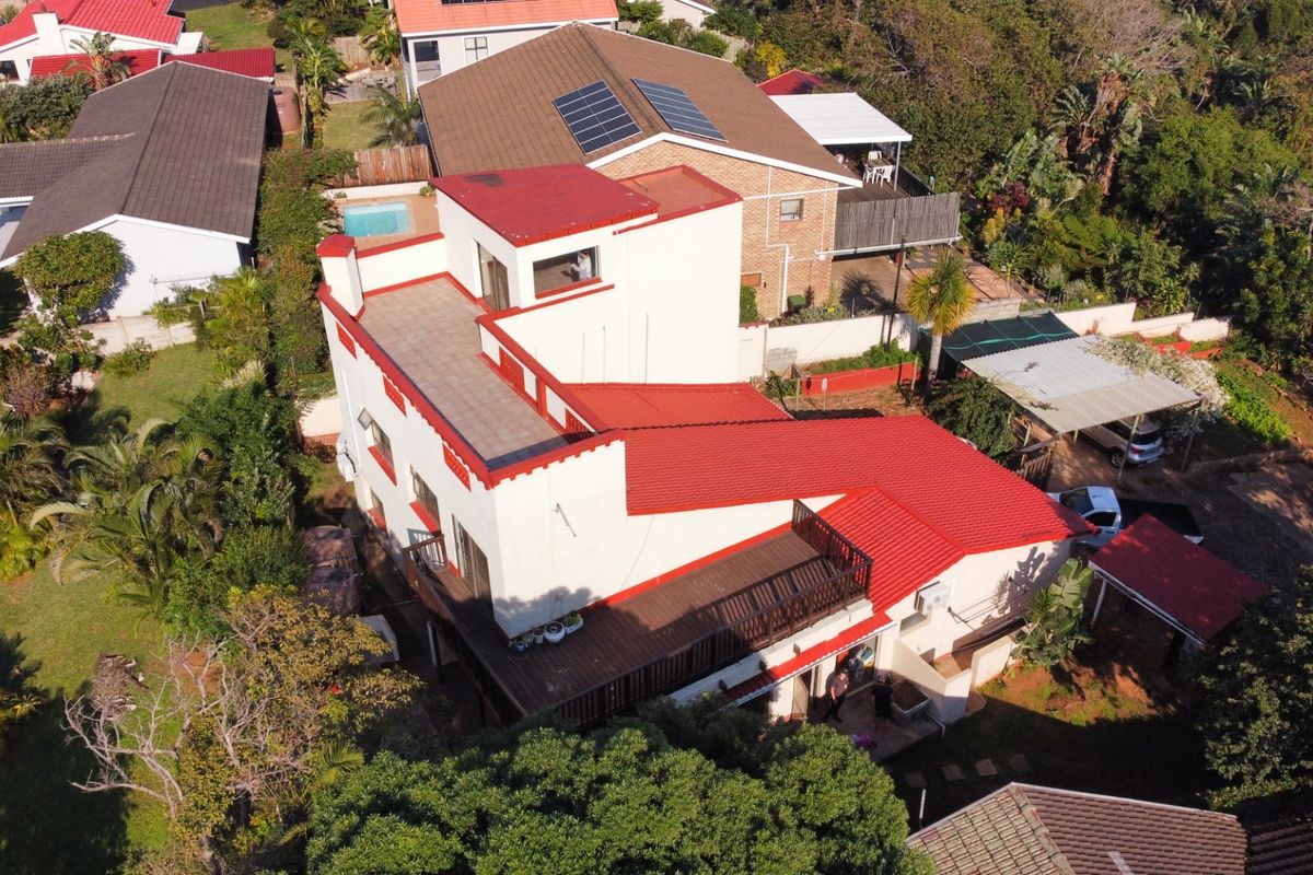 Aerial view of a multi-level residential property featuring a red tiled roof, upper-level balcony, and surrounding garden area.