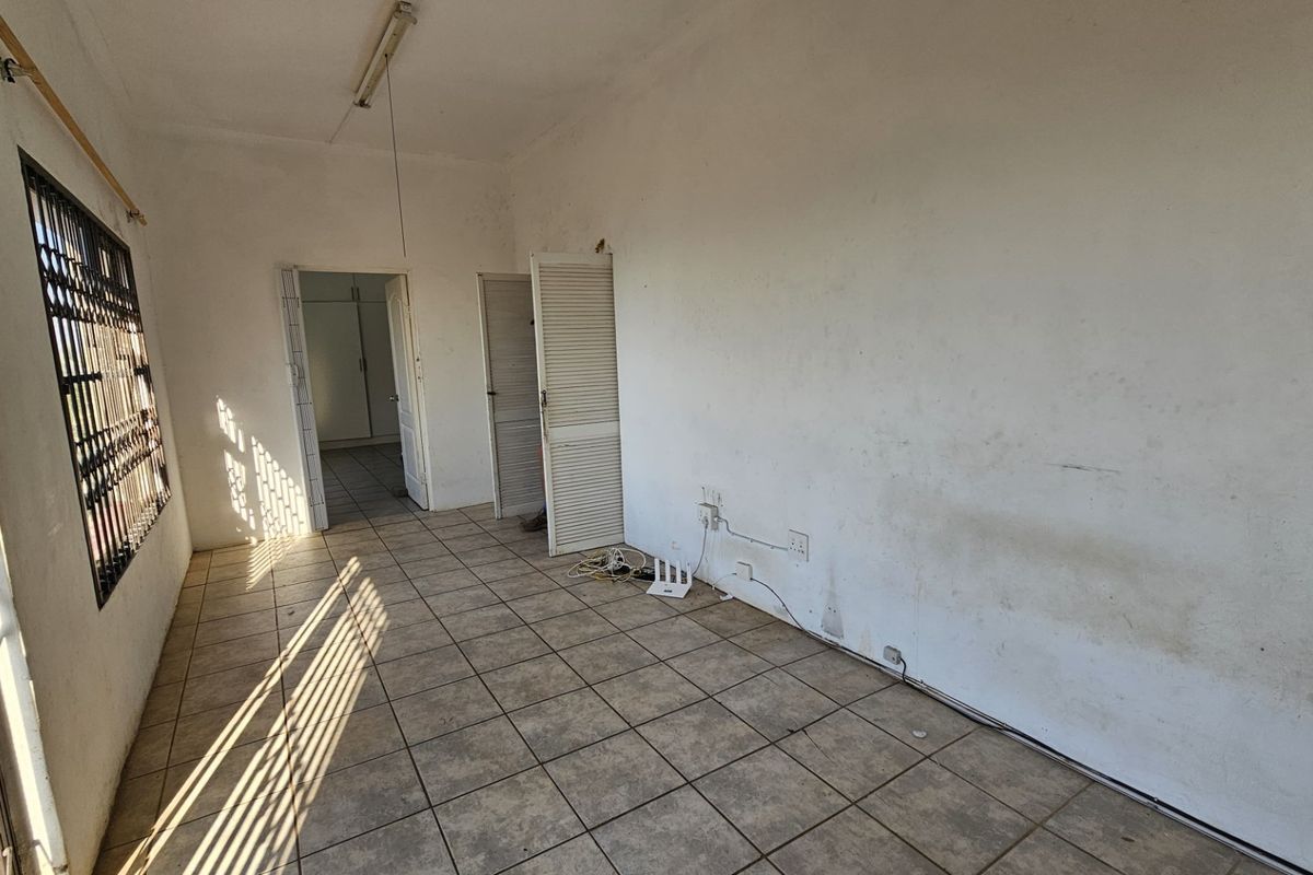 An empty living area featuring tiled flooring, louvered doors, and security bars on the window, requiring cosmetic updates to the walls and finishes.