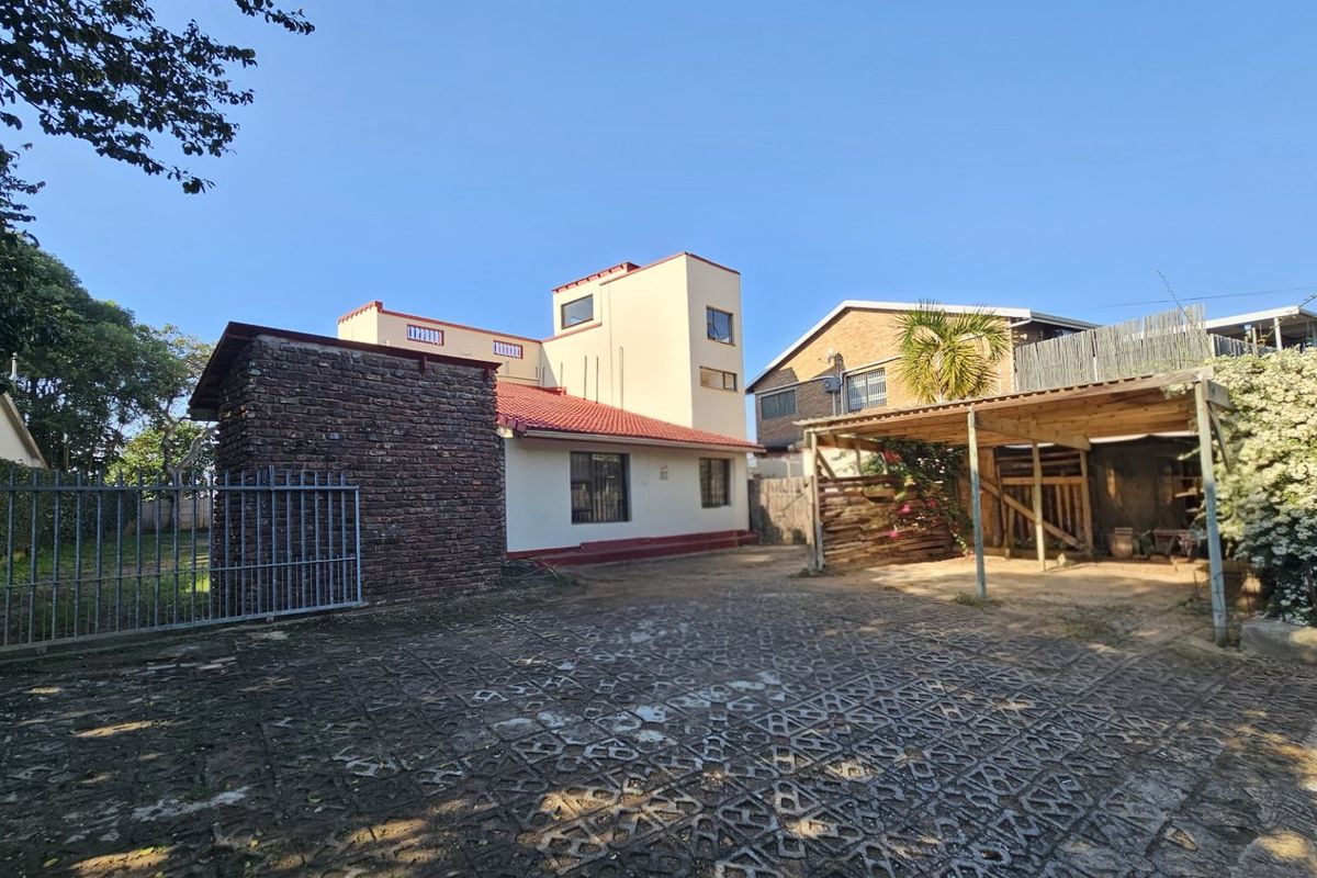 Rear view of the property featuring a multi-level house, paved driveway, and a covered carport area.