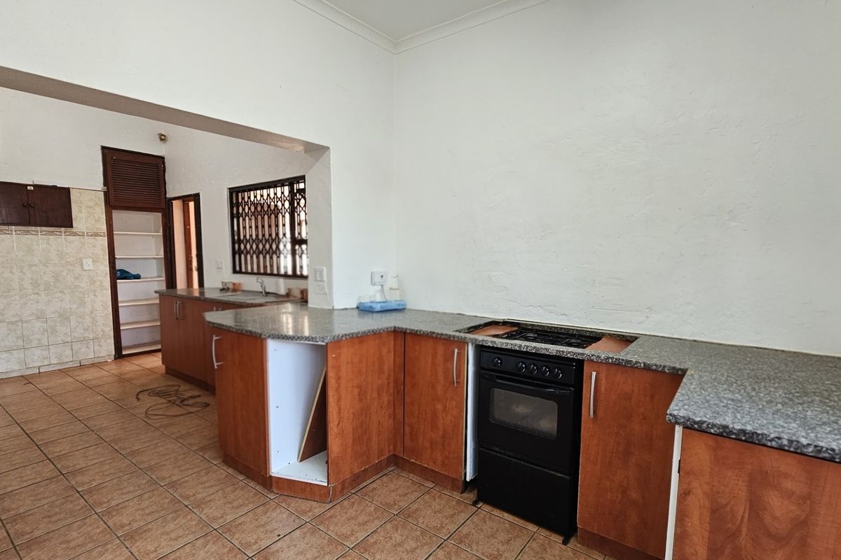 A dated kitchen featuring wood-finish cabinetry, laminate countertops, and a freestanding oven, with tiled flooring and an adjacent pantry area.
