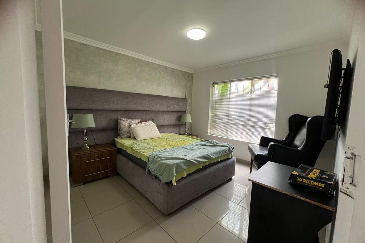 A bedroom featuring tiled flooring, a textured accent wall, and a window fitted with horizontal blinds.